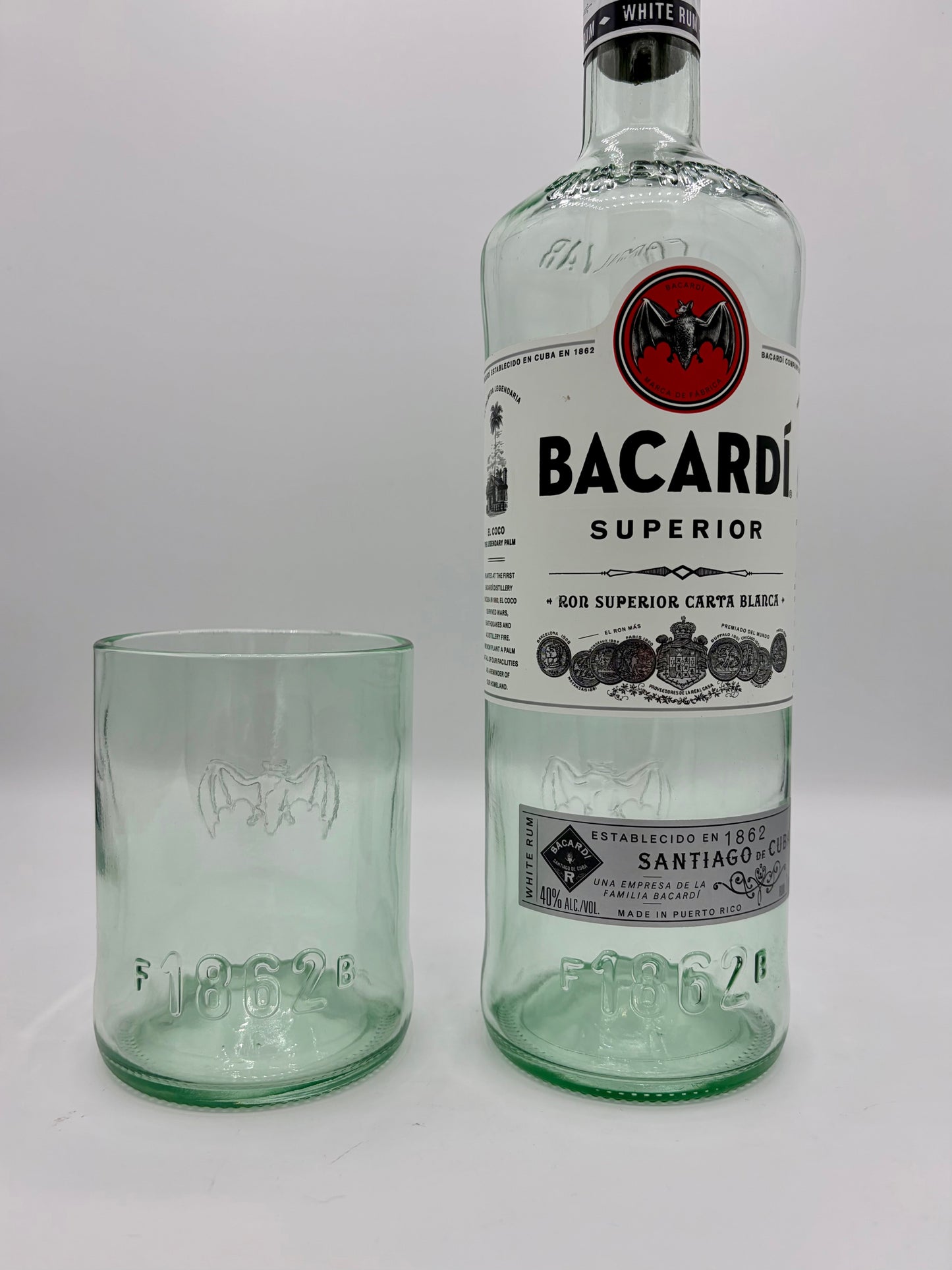 Broken Arrow Glass Recycling upcycled Bacardi tumbler glass with embossed bat logo next to a matching glass bottle.