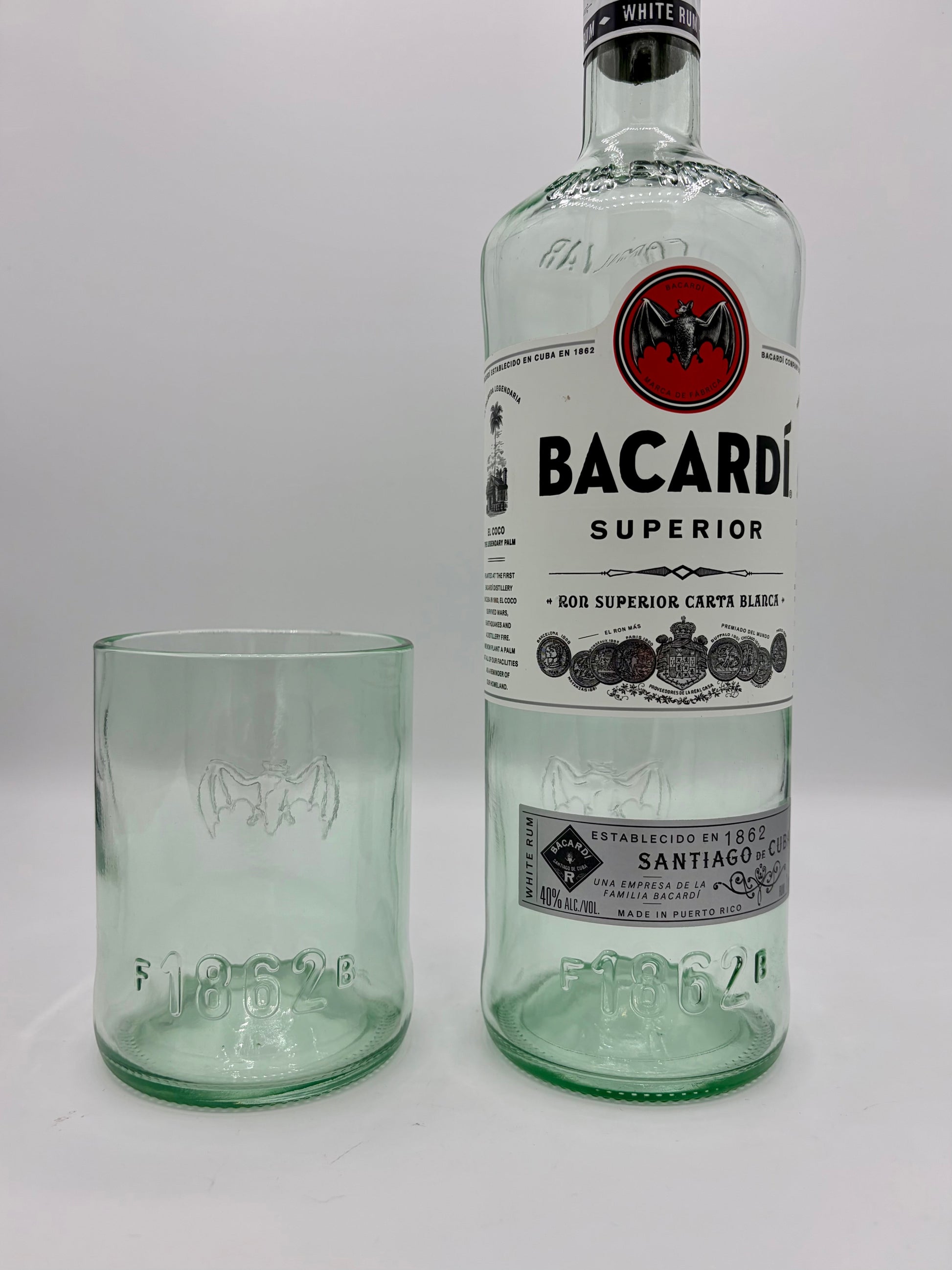 Broken Arrow Glass Recycling upcycled Bacardi tumbler glass with embossed bat logo next to a matching glass bottle.