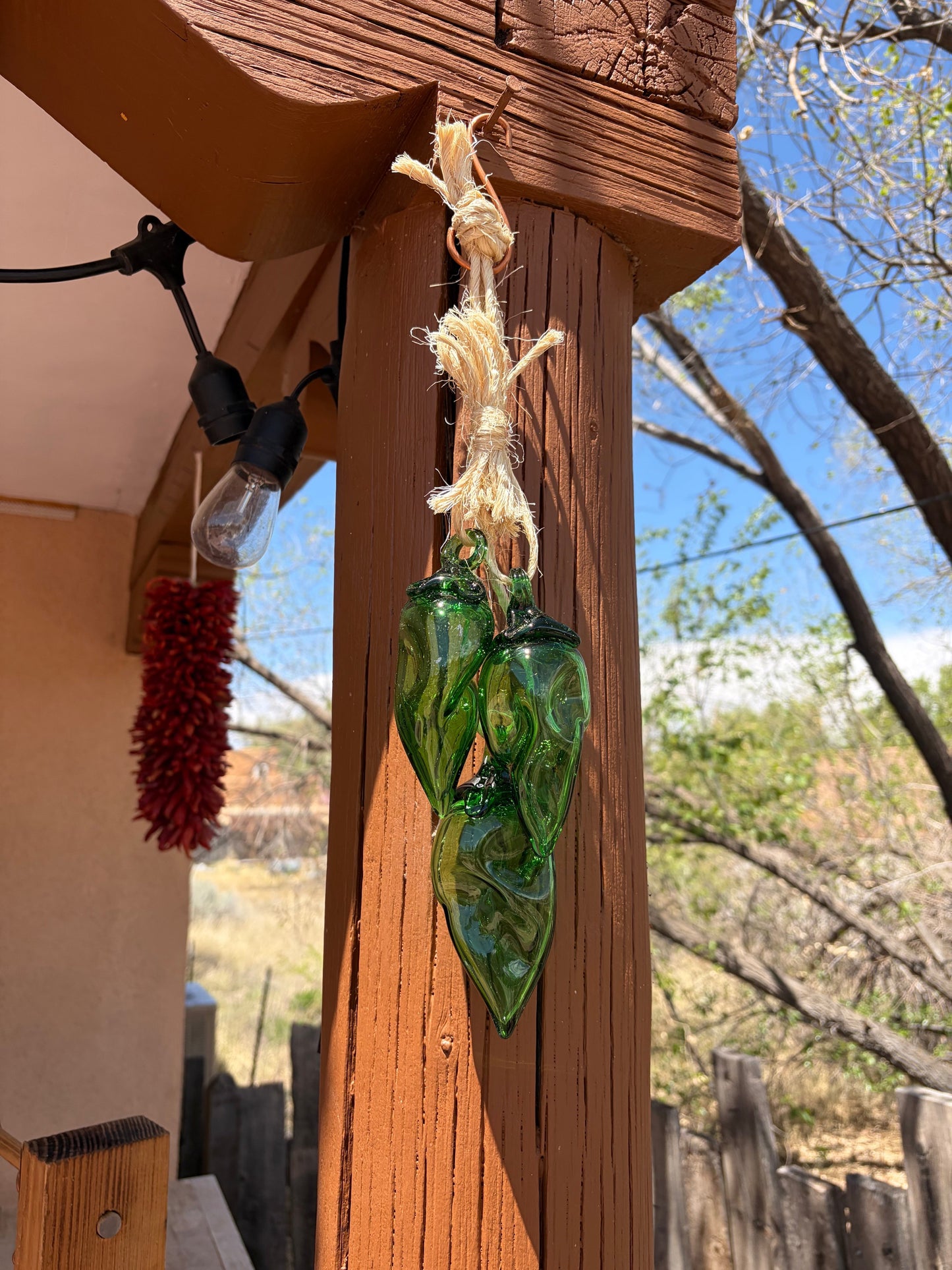 Broken Arrow Glass Recycling handcrafted emerald green glass Chile pepper ristra hanging on a wooden porch post